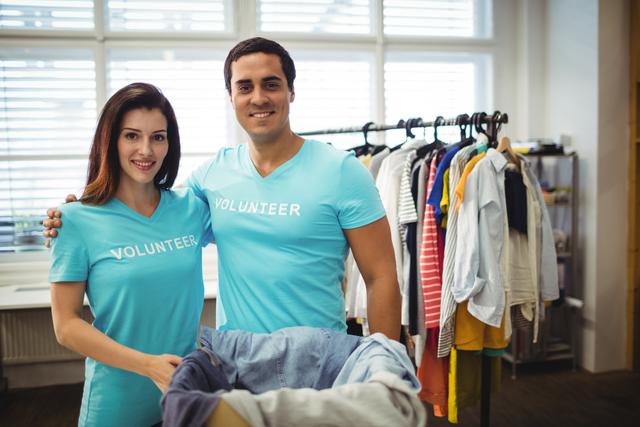 Happy volunteer couple standing with a donation box filled with clothes in a workshop. Ideal for use in content related to charity, community service, volunteering, nonprofit organizations, and social work. Perfect for illustrating teamwork, philanthropy, and giving back to the community.