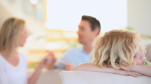 Sad Child on Sofa While Parents Argue in Background