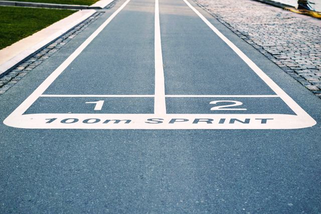100m sprint running track lanes painted on a paved street, perfect for promoting athletic events, sports competitions, outdoor racing, or fitness activities. Use in advertisements, posters, social media, or websites related to sports and athletics.