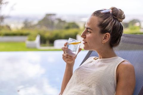 Woman relaxing on sun lounger by poolside sipping citrus water on summer terrace