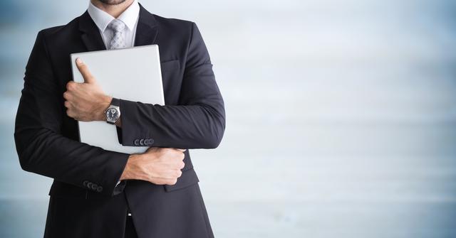 Professional businessman in formal suit holding laptop with blurred background. Perfect for business blogs, corporate websites, technology services promotion, and office-related presentations.
