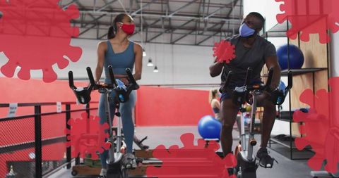 Masked cyclists riding stationary bikes on mezzanine gym promoting safe socially distanced fitness