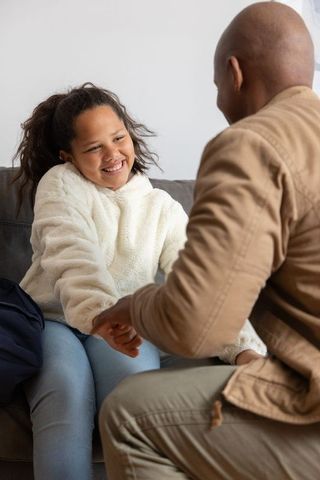 Father holding hands with smiling daughter on couch showing warm family bond