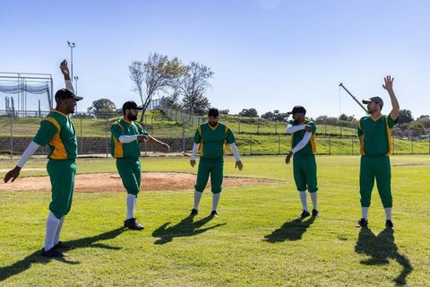 Diverse baseball team warming up on sunny field wearing green and yellow uniforms