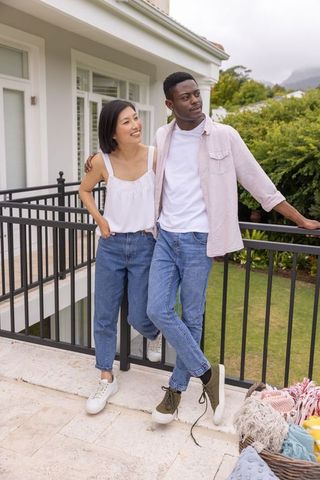 Diverse couple standing on porch smiling and leaning on railing casual denim lifestyle