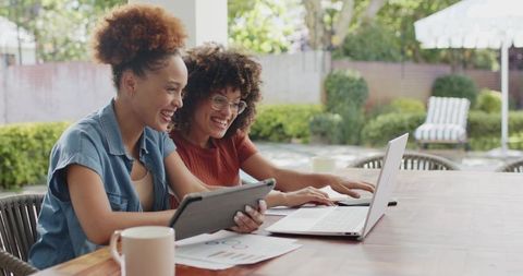 African American Women Collaborating Outdoors Using Laptop and Tablet on Backyard Patio