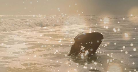 Backlit silhouette kneeling in surf at golden hour coastal reflection peaceful beach serenity