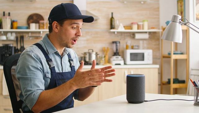 Man talking to smart speaker in kitchen using voice assistant for hands-free control