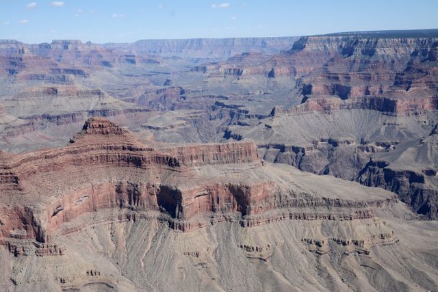 Grand Canyon's majestic rock formations display variations in color and depth, making it a popular travel destination. This image highlights the vast, rugged terrain under a clear sky, ideal for use in travel and tourism promotions, educational materials on geology and natural landscapes, and adventure-themed advertising campaigns.