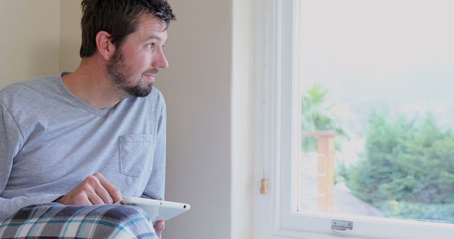 Man in Loungewear Looking Out Window with Tablet - Download Free Stock Images Pikwizard.com