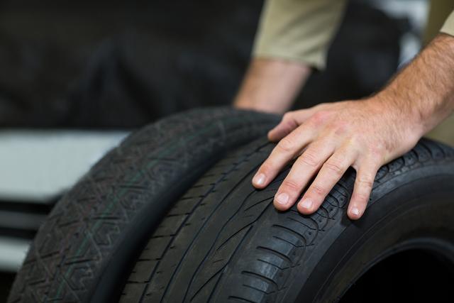 Mechanic inspecting car tires in a repair garage, focusing on tire tread and condition. Useful for illustrating automotive maintenance, vehicle safety checks, and professional repair services. Ideal for websites, blogs, and articles related to car maintenance, tire care, and automotive workshops.