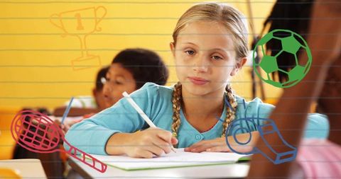Blonde student concentrating while writing in classroom with colorful sports doodles