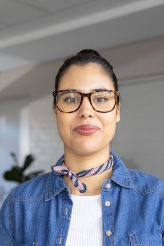 Smiling professional woman wearing tortoiseshell glasses and denim shirt in modern office