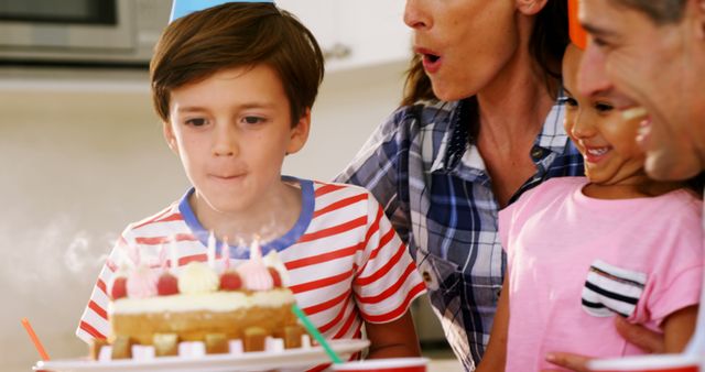 Boy blowing out candles on birthday cake with family surrounding, celebrating special occasion with loved ones. Perfect for illustrating family gatherings, children's parties, and joyful moments.