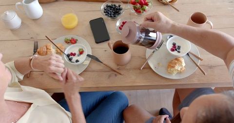 Diverse couple sharing cozy breakfast while pouring coffee from french press overhead