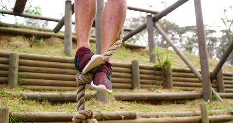 Man balancing on braided rope with maroon sneakers on wooden terraced obstacle course