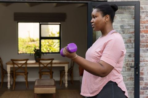 African american woman lifting dumbbell at home doorway for strength and fitness