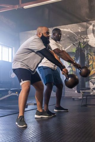 African american men swinging kettlebells in industrial gym partner strength training duo