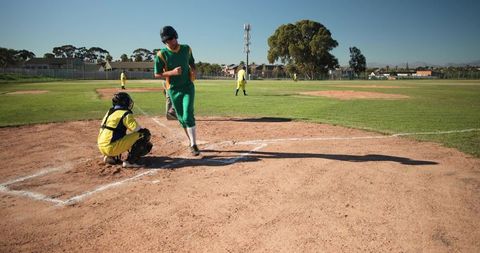 Baseball runner crossing home plate while catcher crouching on sunny community field