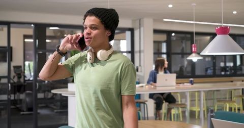 Young african american man talking on smartphone with headphones in modern coworking space