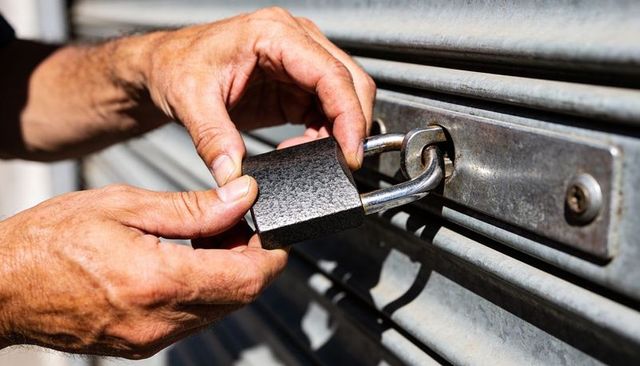Hands locking heavy-duty padlock on metal roll-up shutter for commercial security