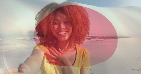 Smiling woman taking beach selfie wearing yellow top and holding phone with red overlay
