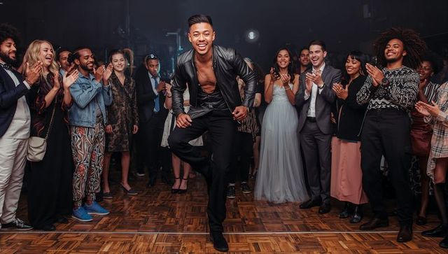 Asian dancer performing high step in leather jacket on parquet floor during celebration