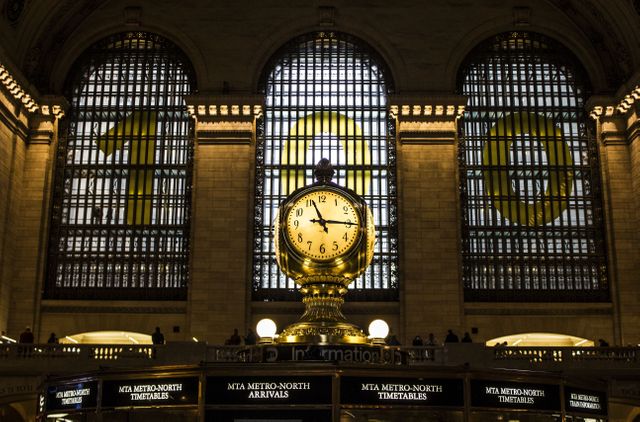 Grand Central Station's iconic clock lit up at night in celebration of its 100-year anniversary. The grandiose architecture and golden hue of the clock create a mesmerizing scene. This image is perfect for travel-related content, historic landmark features, architectural studies, or New York City-themed promotions.