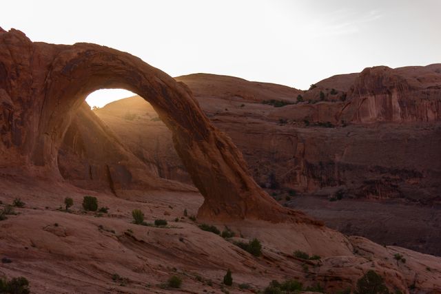 Capturing a stunning natural rock arch with sunlight filtering through at twilight in a desolate desert landscape. Ideal for use in travel blogs, geological study resources, adventure tourism marketing, and nature photography collections.
