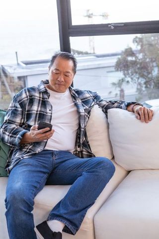 Man relaxing on sofa with smartphone overlooking scenic harbor