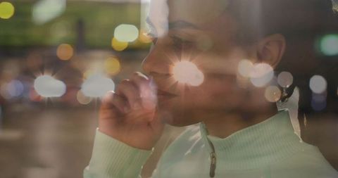 Pensive woman looking out window at night with urban bokeh reflections and glow