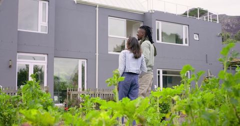Diverse couple standing by raised garden beds in front of modern gray two-story home