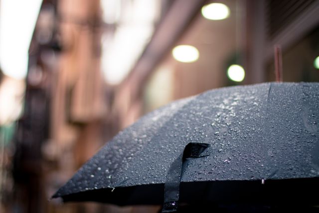 Black umbrella covered with raindrops on a rainy city street. Suitable for illustrating urban weather, street photography, rainy day themes, and scenes of personal protection in wet conditions.