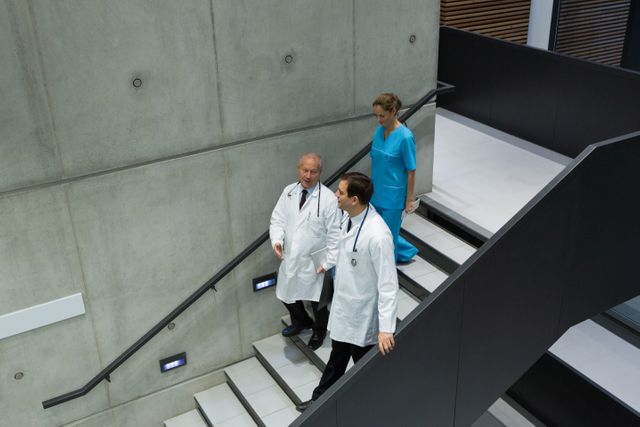 Doctors and a surgeon are seen interacting on a staircase in a modern hospital. This image can be used to depict teamwork and collaboration among medical professionals, suitable for healthcare websites, medical articles, and hospital brochures.