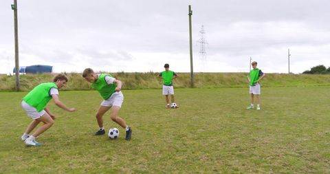 Teenage Boys Practicing Soccer Skills on Field with Green Bibs