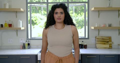 Indian woman standing in sunlit modern kitchen with marble countertop and greenery view