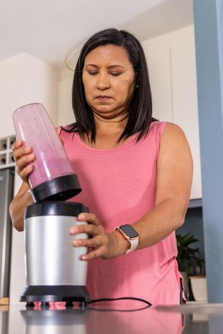 Asian woman preparing pink smoothie with personal blender at modern kitchen counter