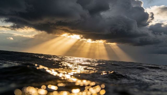Sunbeams breaking through storm clouds over ocean, golden rays illuminating dark waves