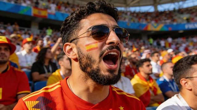 Passionate spanish football fan cheering in stadium with face paint and sunglasses