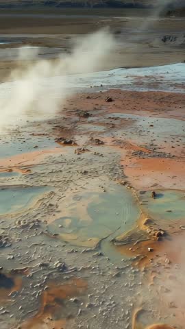 Vertical geothermal video of bubbling mud domes releasing steam and colorful thermal pools
