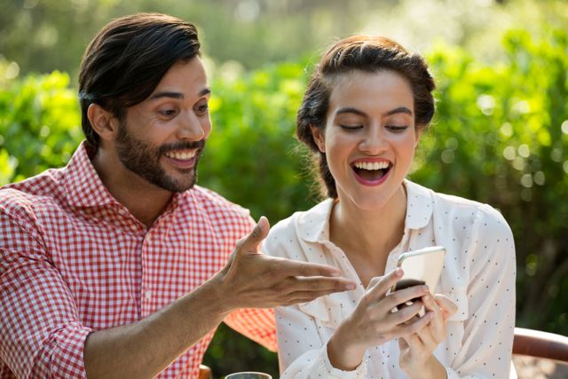 Happy young couple using smart phone together at park