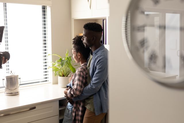 Thoughtful african american young couple looking through window while standing in kitchen at home. copy space, unaltered, lifestyle, home, love and togetherness concept.