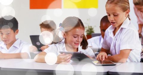 Elementary students using tablets and collaborating at classroom desks for digital learning