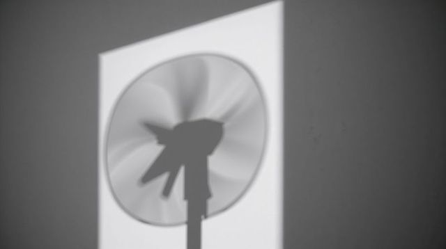 Monochrome Motion: Rotating Fan Silhouette Projecting Shadow on Minimal Wall with Radial Blur