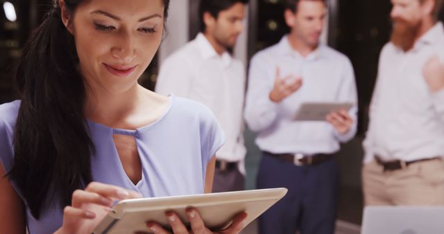 Businesswoman Using Tablet in Office with Colleagues in Background - Download Free Stock Photos Pikwizard.com