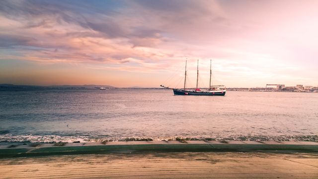 Sailing vessel on calm waters during sunset with beautiful, vibrant sky and soft horizon. Ideal for travel websites, nautical themes, coastal living promotions, scenic backgrounds for presentations, or relaxation themes in wellness campaigns.