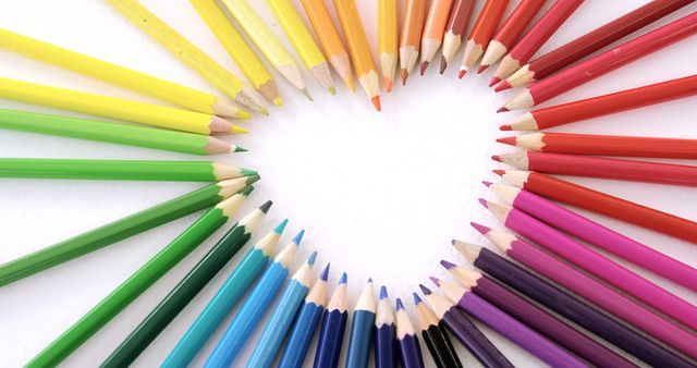 Colored pencils are arranged in a circle creating a heart shape on a white background, with copy space. This arrangement symbolizes creativity and love for art, making it ideal for educational and artistic concepts.