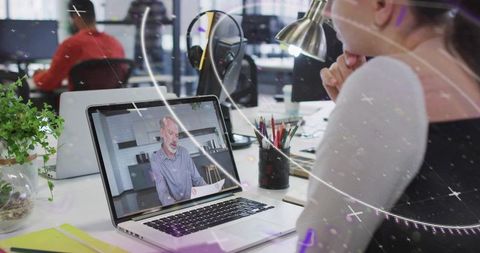Woman watching virtual presentation on laptop in open office collaborative team workspace