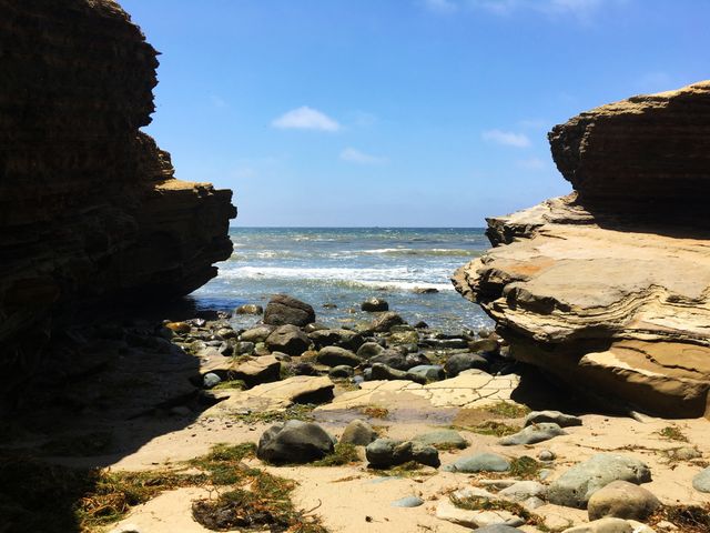 Natural seaside scenery showing serene rocky beach cove on sunny day. Ideal for coastal landscape features, environmental conservation topics, travel advertisements, and relaxation themed projects.