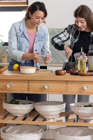 Two friends preparing citrus and herbs at wooden kitchen island using mortar and pestle